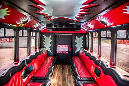 Interior of a bus with red and black leather seats and vibrant red lighting. The floor is wooden, creating a lively and modern atmosphere.